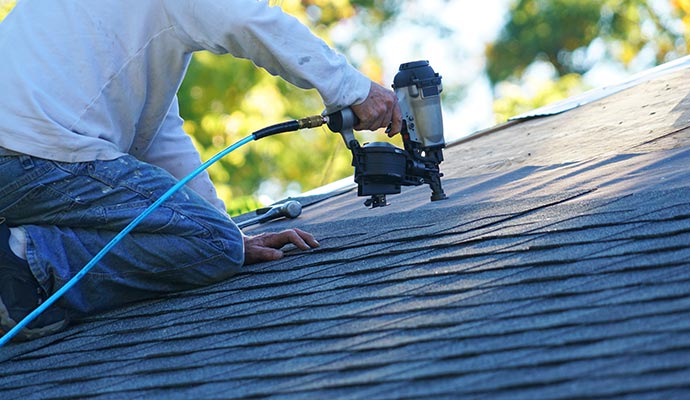 handyman using nail gun to installing shingle roof