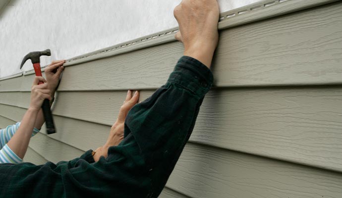 worker installing siding on a house