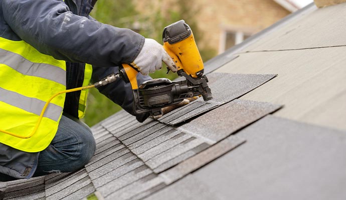 workman using pneumatic nail gun install missing shingles roof