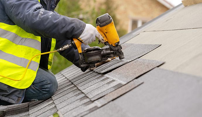 workman using pneumatic nail gun install tile on roof of residential home